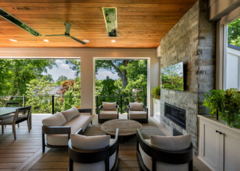 Covered porch seating area with a stone fireplace and woodland views
