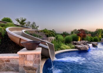 Curving waterslide integrated into planted boulders above the pool