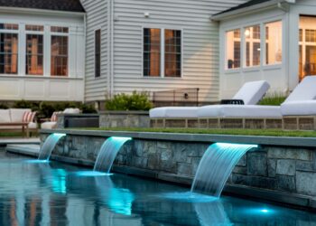 Illuminated pool water features beside terrace seating at dusk
